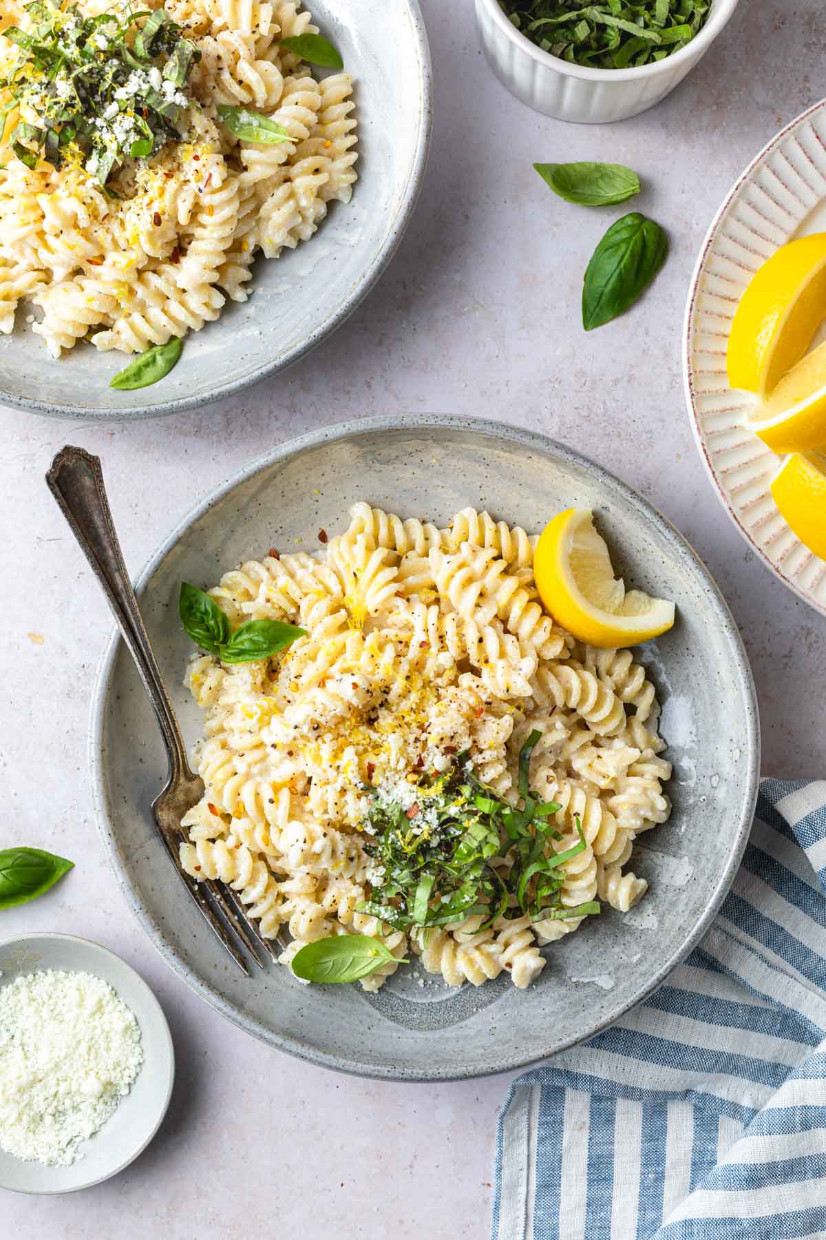 A bowl of fusilli topped with sliced basil, lemon zest and lemon slices