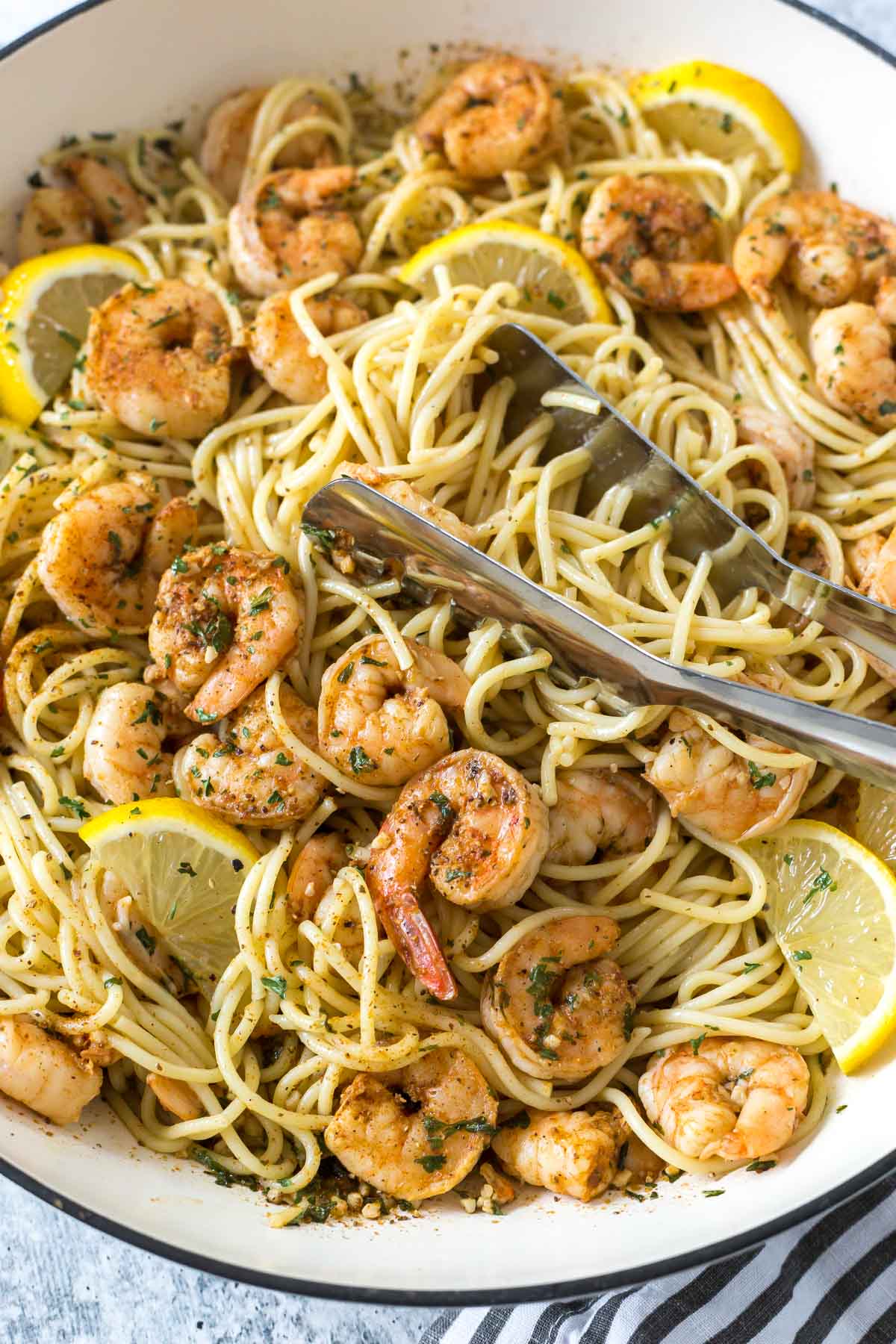 A bowl of shrimp scampi pasta with lemons all mixed up in a bowl with pasta pullers.
