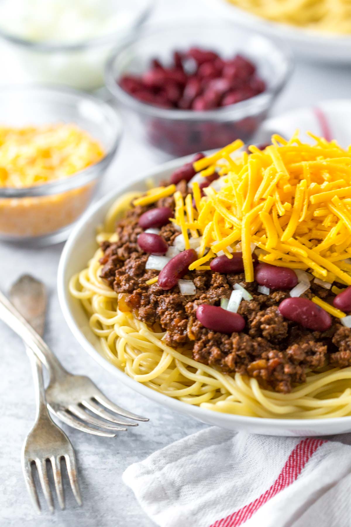 chili spaghetti in a white bowl topped with onions beans and cheese