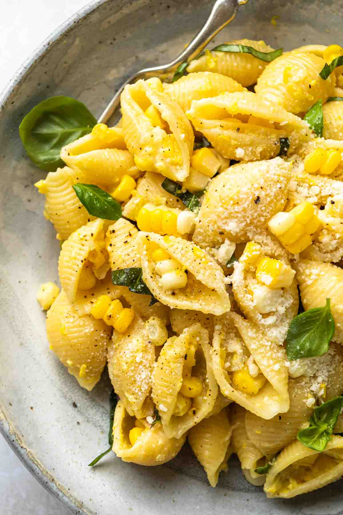Close up of corn pasta, showing the corn kernels, garnished with grated parmesan cheese, black pepper and fresh basil leaves. 