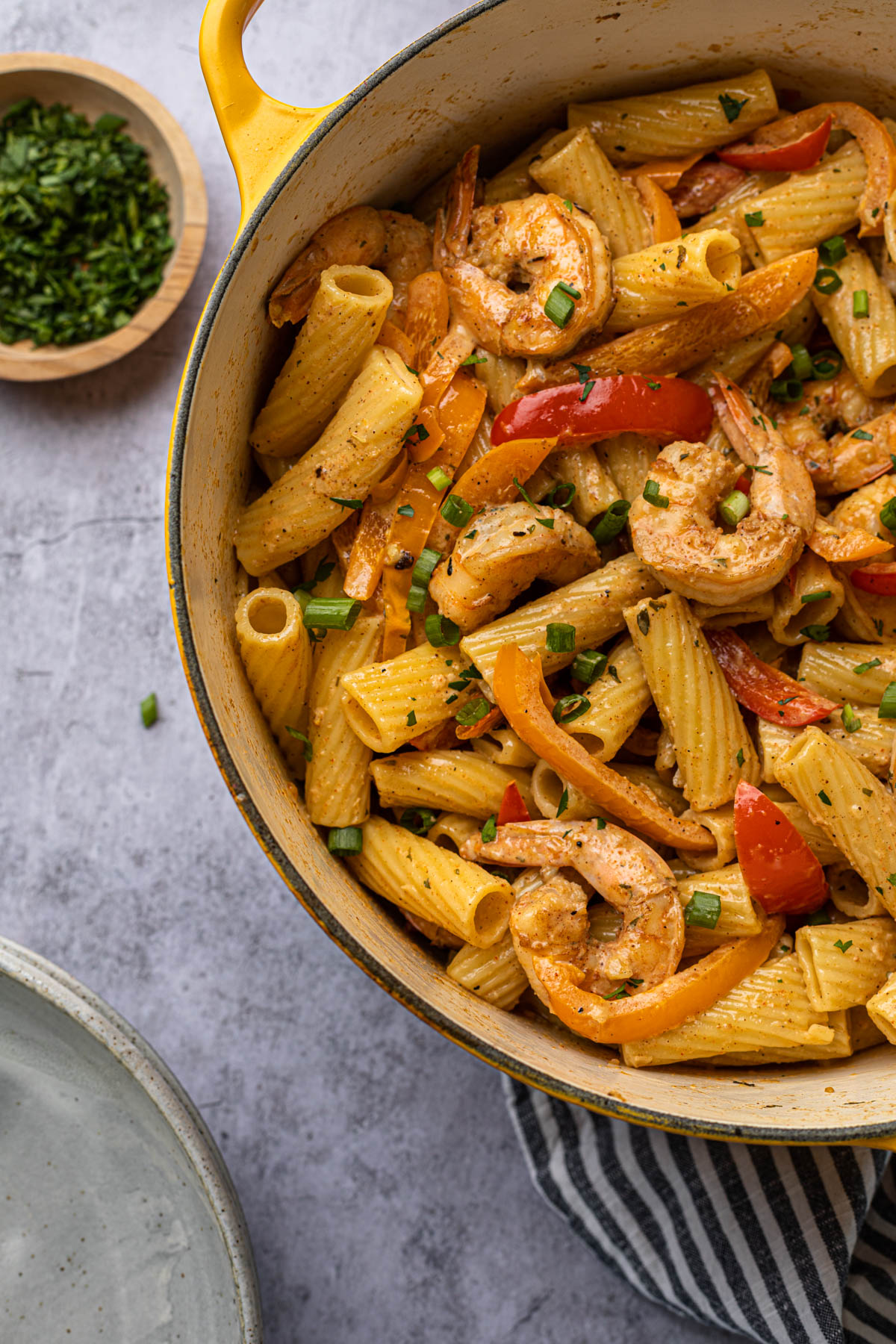 A dutch oven full of pasta, shrimp and bell peppers with a creamy jamaican sauce. 