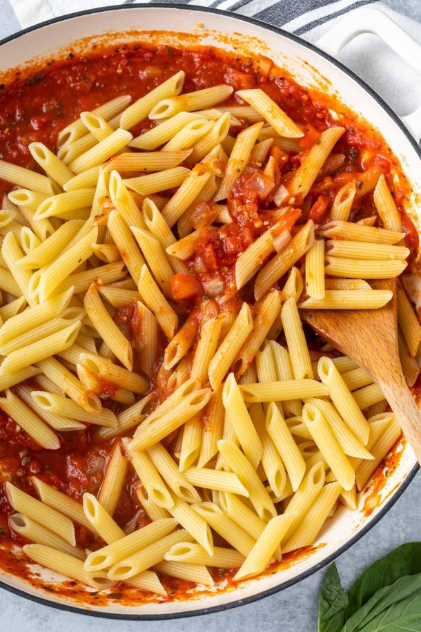 Penne pasta being stirred into arrabiata sauce. 