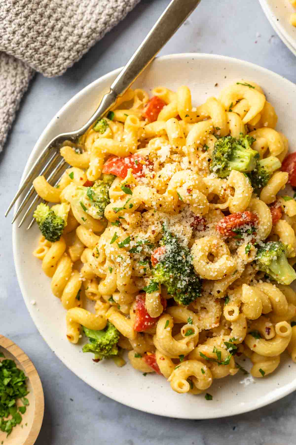 Hummus pasta with broccoli and roasted red peppers on a plate with a fork. 