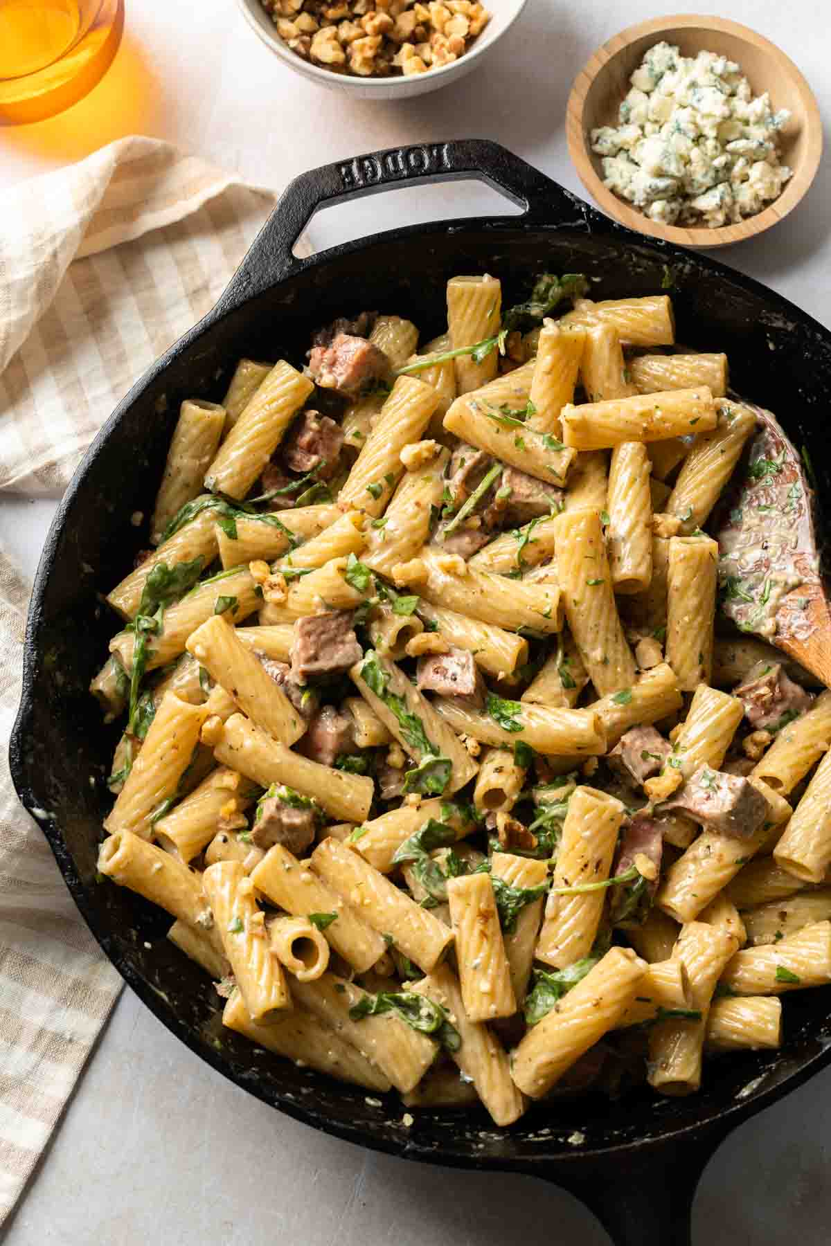 A cast iron skillet full of steak pasta with a wooden spoon in it. 