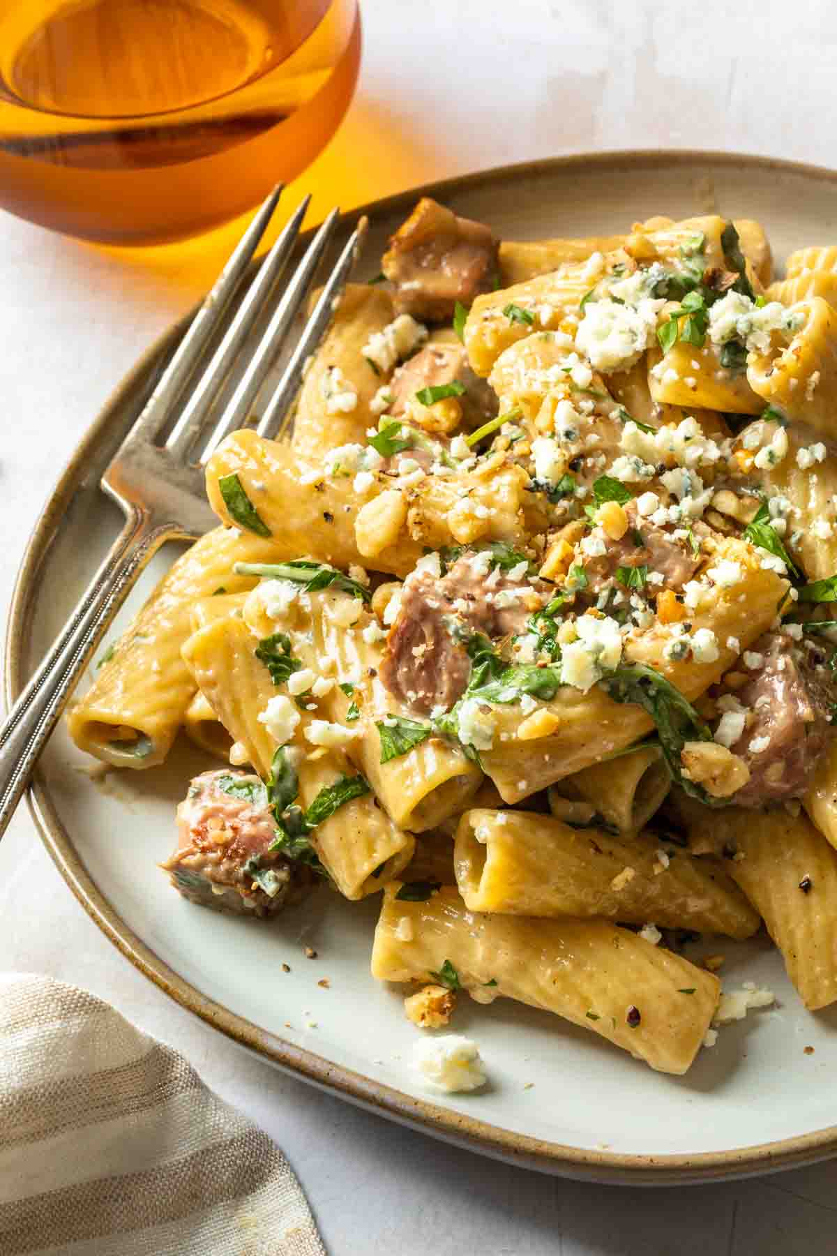 A plate of steak and rigatoni pasta with a gorgonzola cream sauce topped with walnuts and gorgonzola cheese crumbles. 