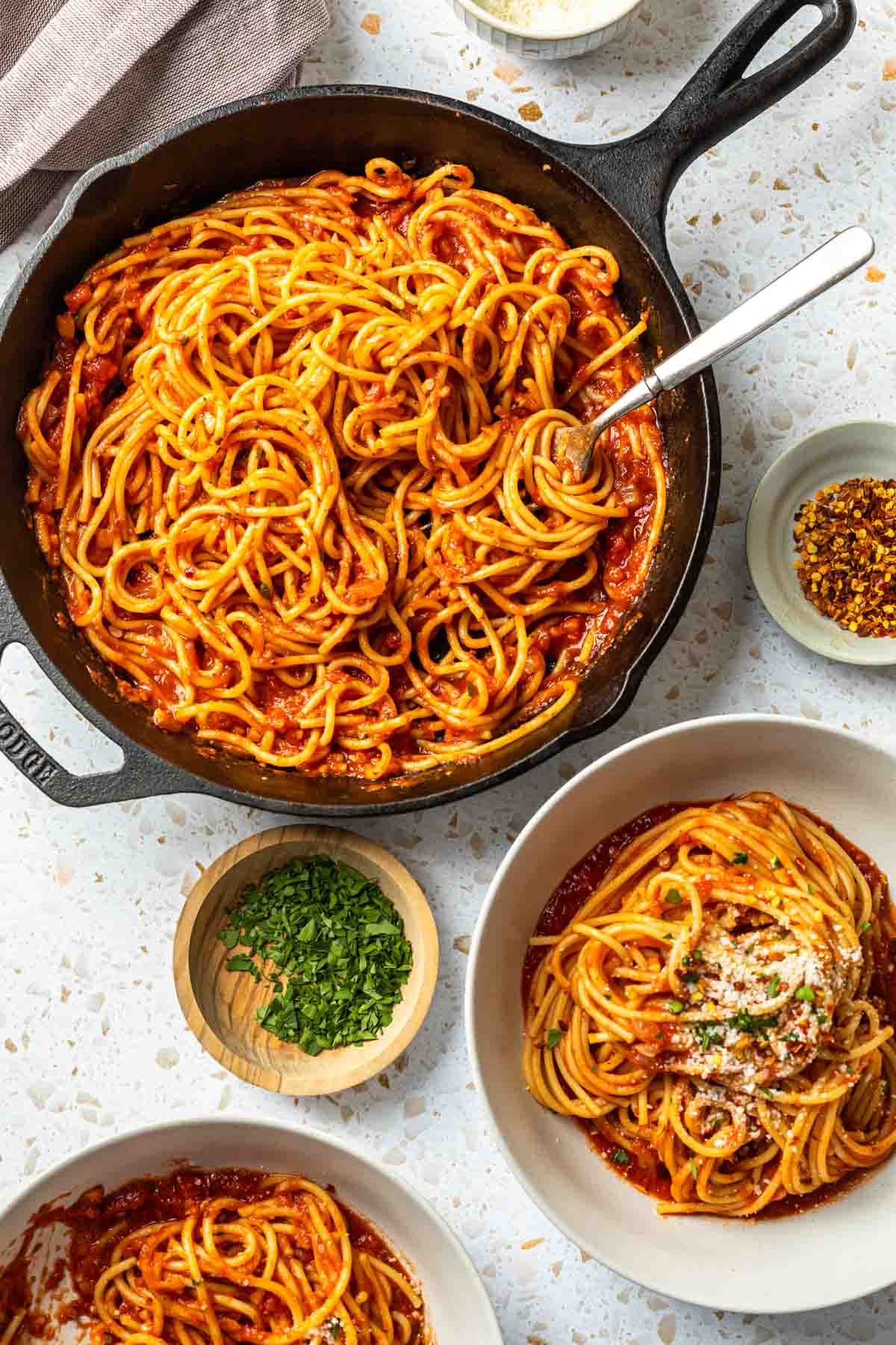 A cast iron skillet with spaghetti arrabbiata and bowls of spaghetti surrounding it. 