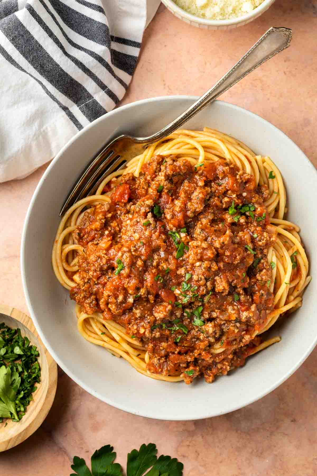 A bowl of spaghetti with meat sauce garnished with fresh parsley. 