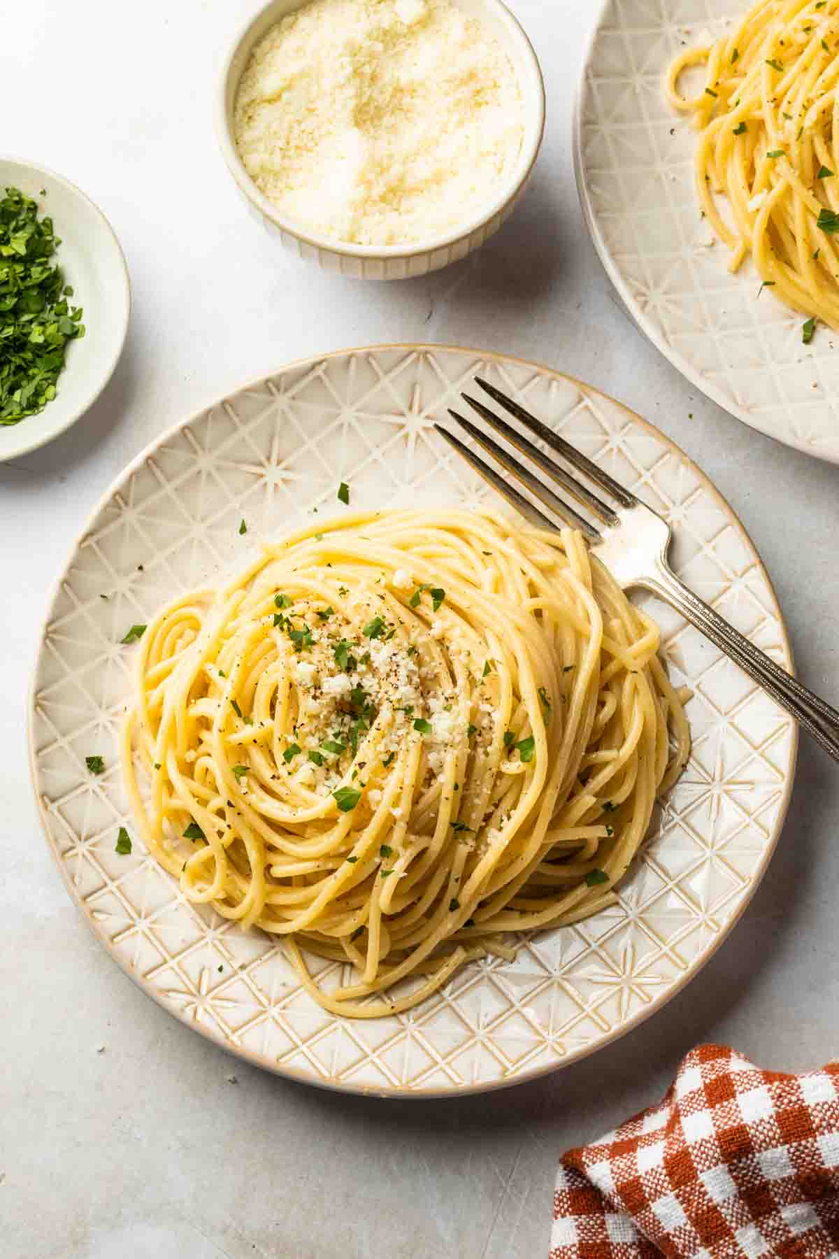 A plate of spaghetti with an oil based sauce, garnished with grated cheese and fresh parsley. 