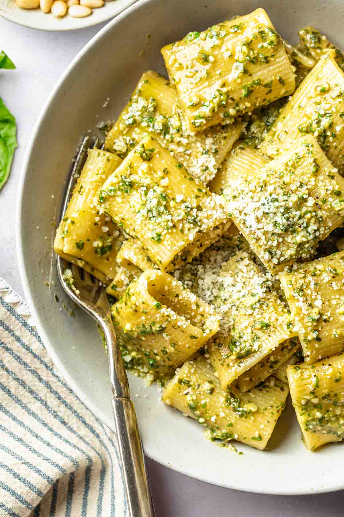A bowl of rigatoni with pesto sauce in a bowl garnished with grated cheese.