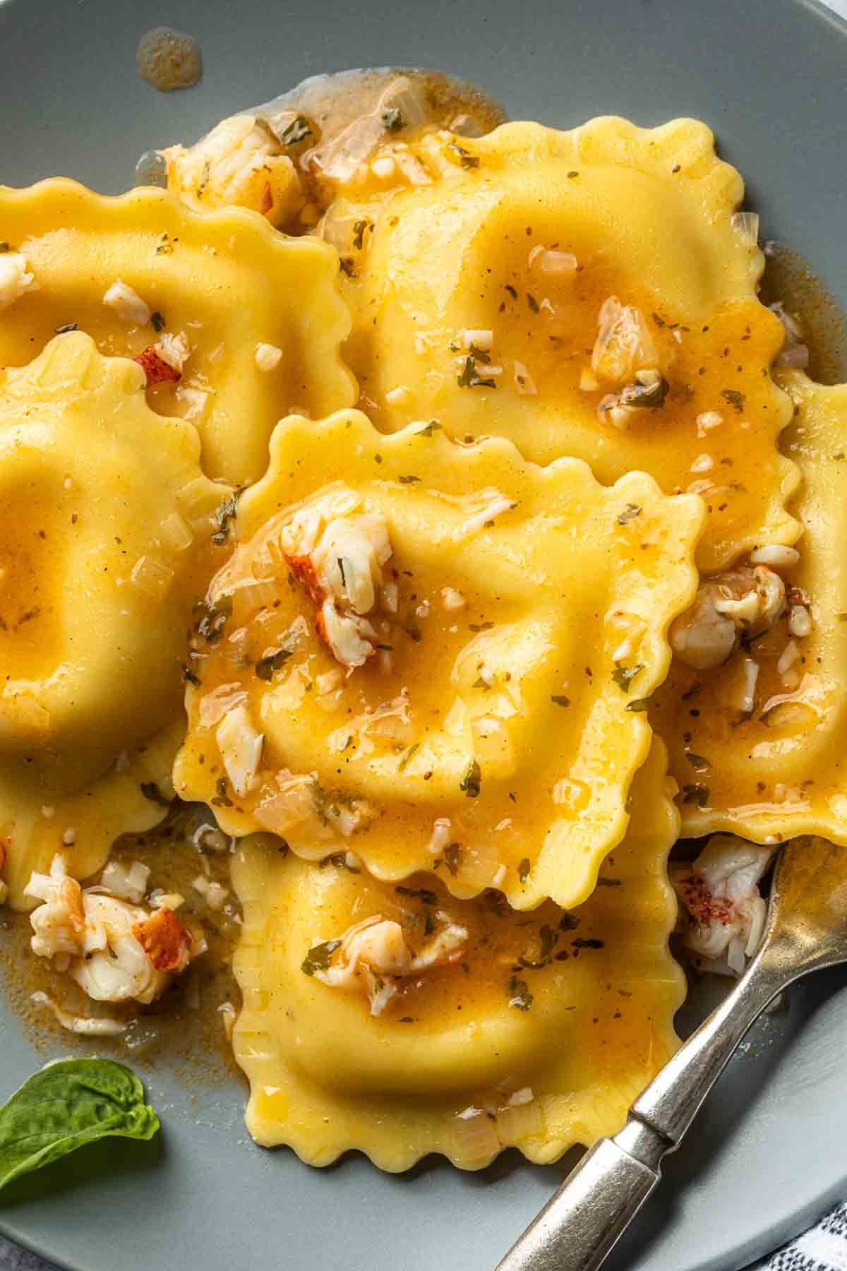 Close up of lobster ravioli on a plate covered in a white wine sauce. 