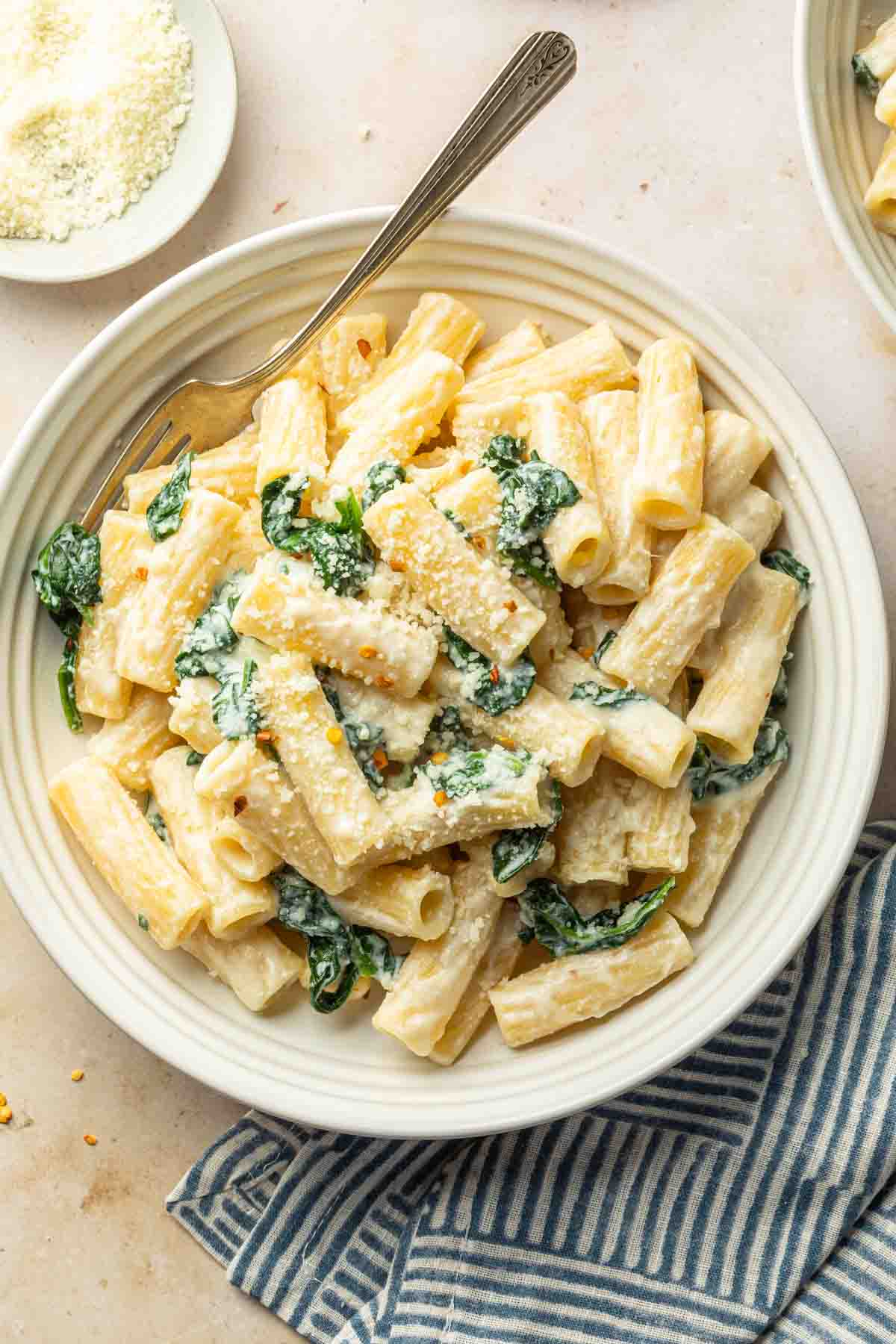 A bowl of spinach ricotta pasta, garnished with grated cheese and crushed red pepper flakes. 