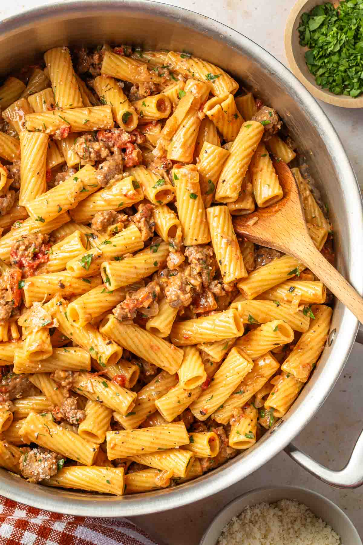 A pot of fennel sausage pasta made with rigatoni with a wooden spoon resting in it. 