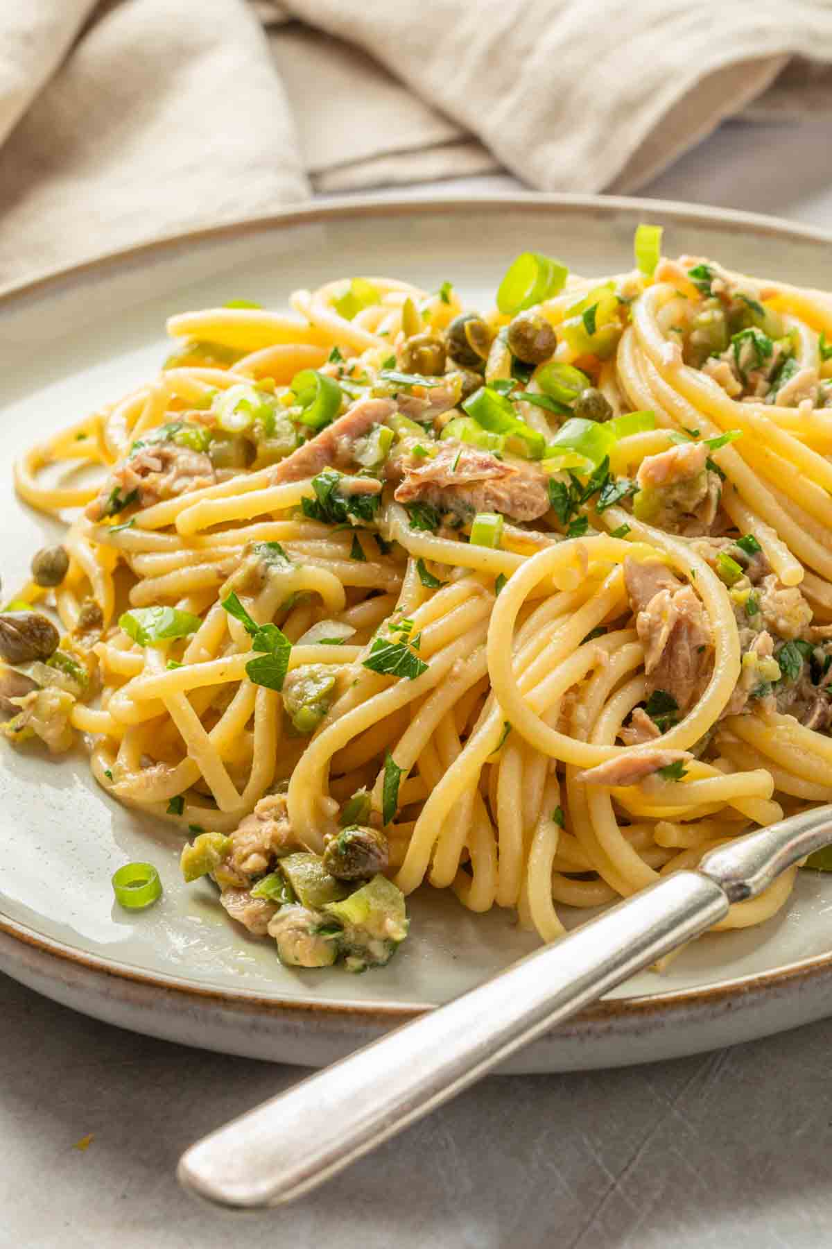 Close up of a plate of pasta made with canned tuna, green onions, olive and capers. 