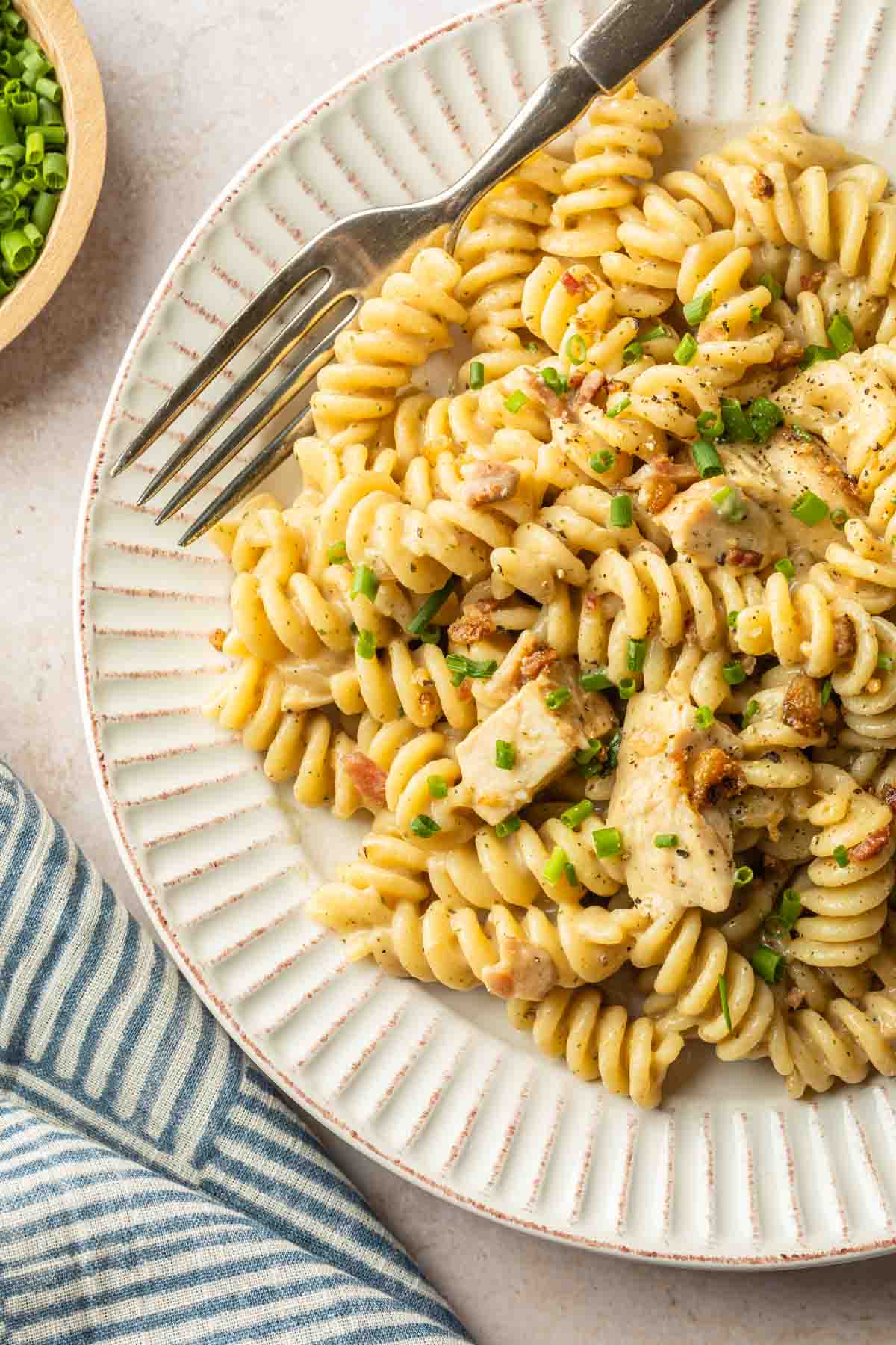 A plate with spiral pasta, in a creamy ranch sauce with chicken and bacon and fresh chives. 