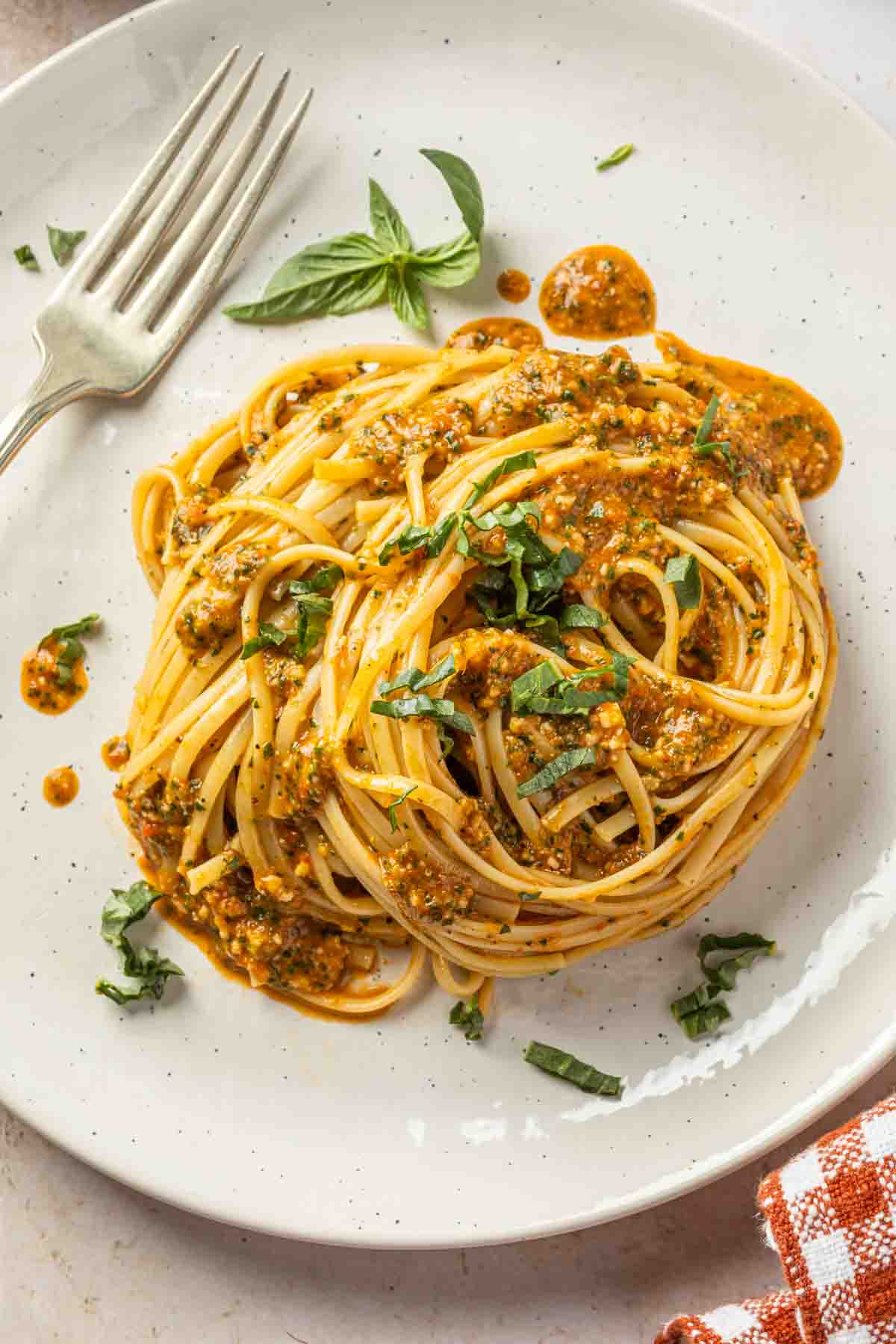 A plate of linguine in a red pepper pesto sauce, garnished with fresh sliced basil leaves. 